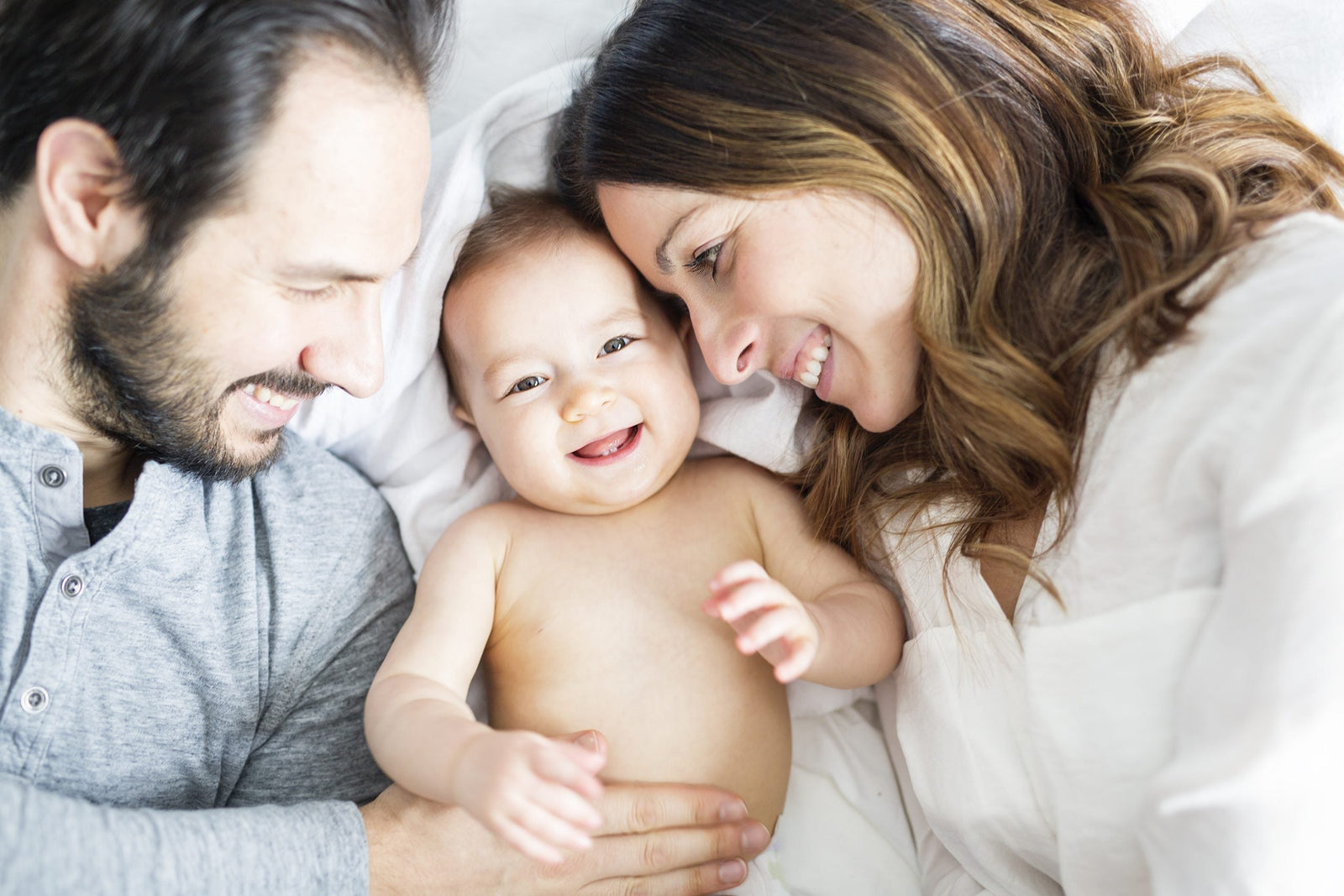 Mutter und Vater mit einem kleinen Baby, die gemeinsam im kuscheln und strahlen.